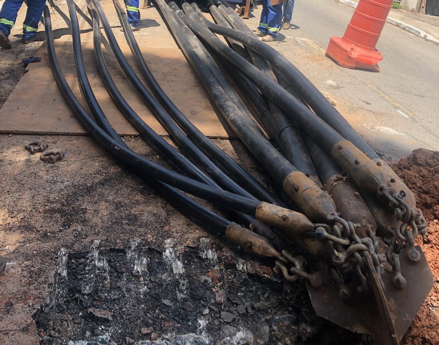 Feixe de dutos com cabeças de puxamento entrando no poço de entrada, em rua urbana